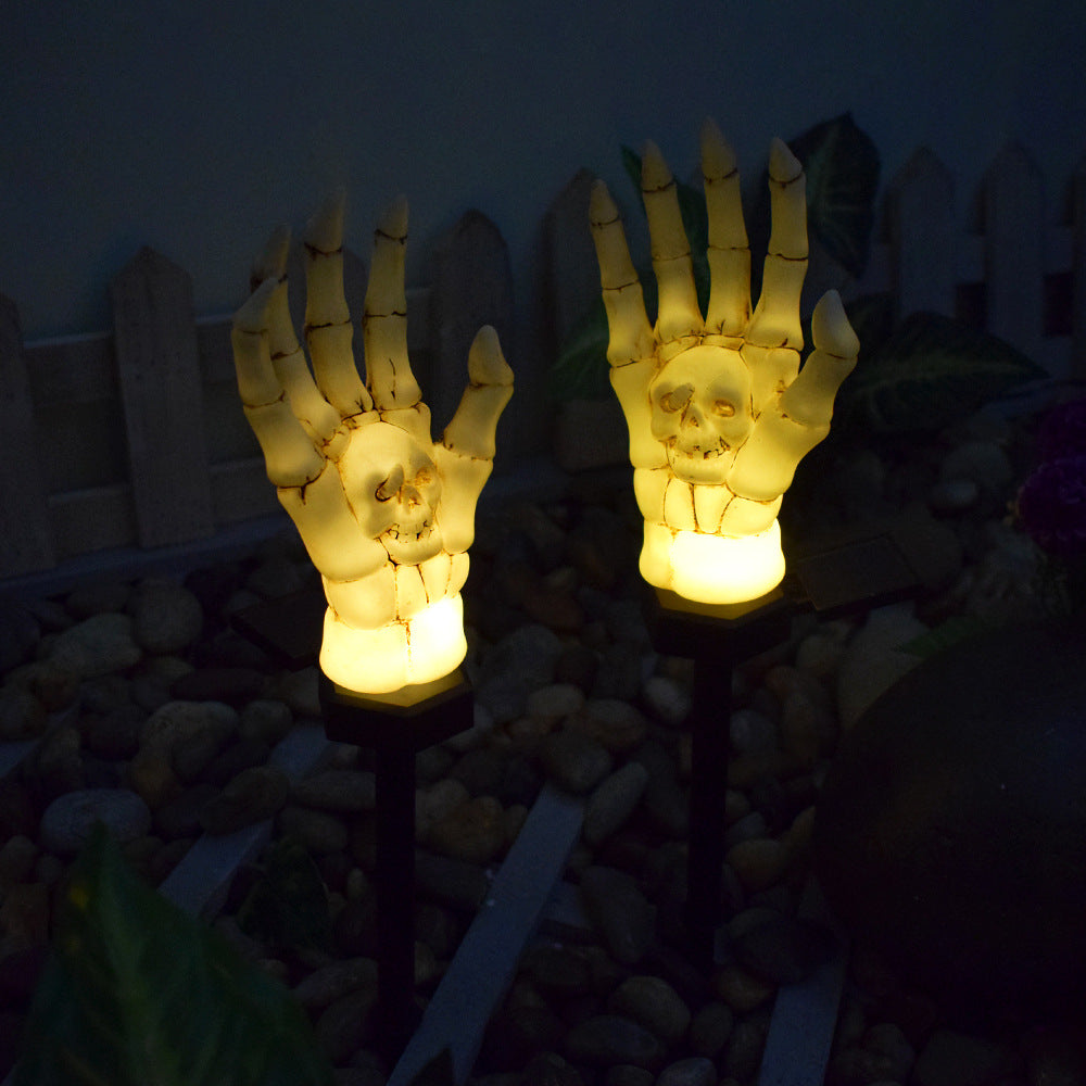 Two skeleton hand stake lights glowing warm amber in a garden after dark