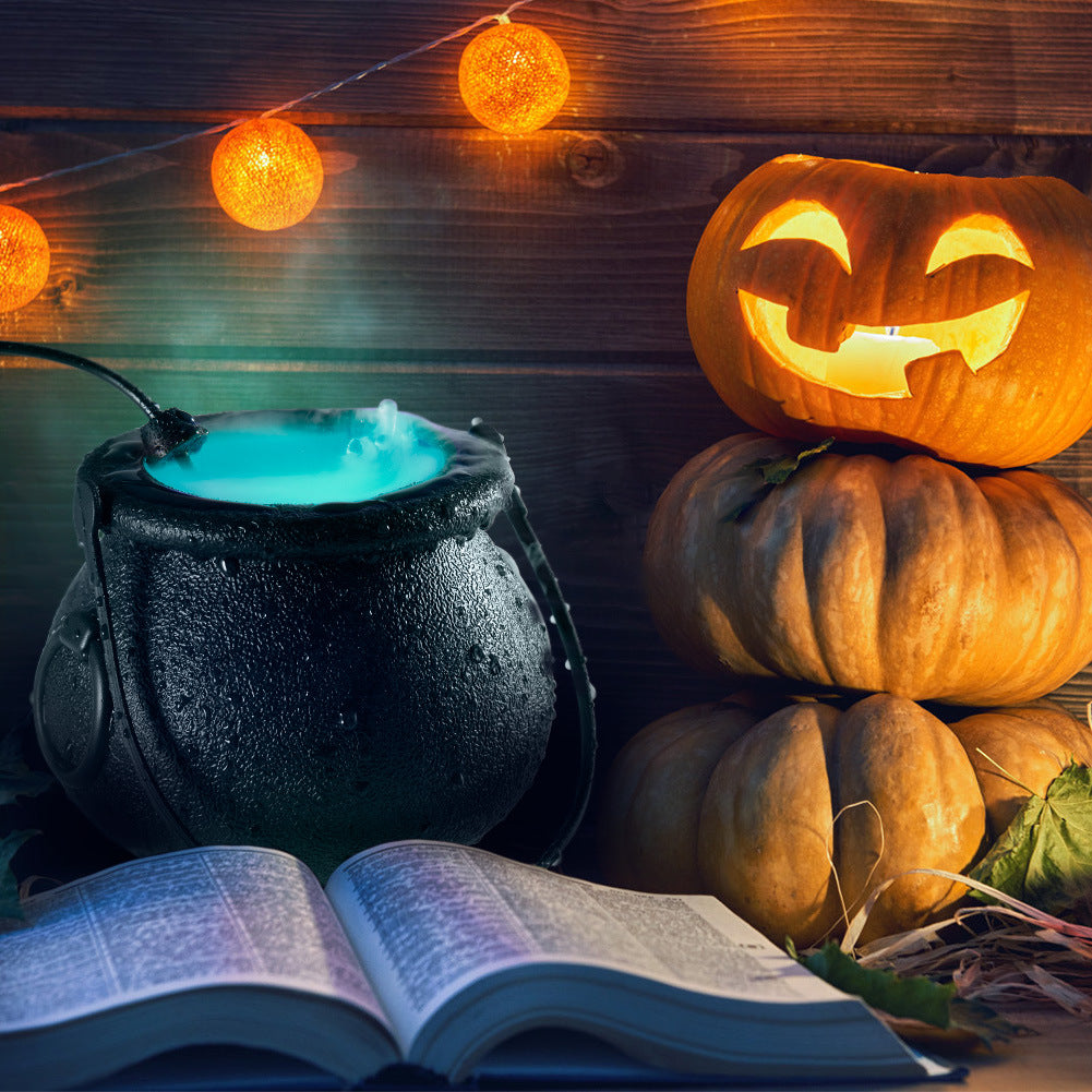Black witch's cauldron misting on a table beside carved pumpkins and string lights